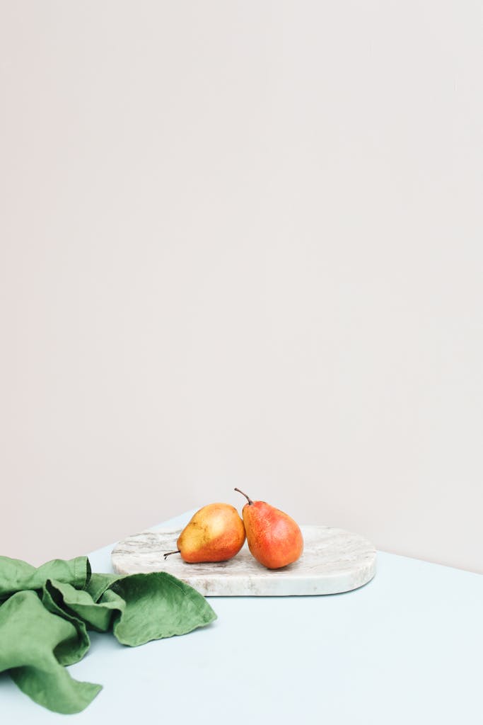 Minimalist composition featuring two vibrant pears on a marble slab with a soft backdrop.